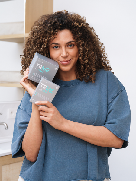Woman holding two 'TRME' products in a kitchen setting