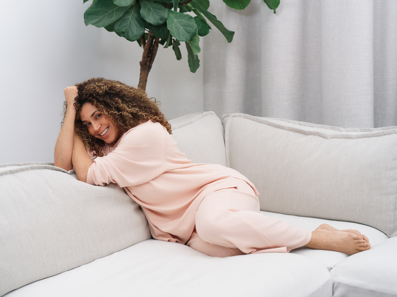 Woman in a pink outfit sitting on a white couch with a plant in the background