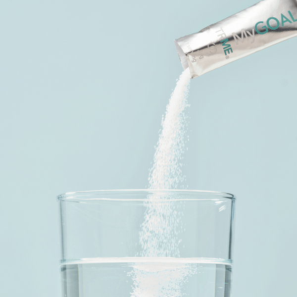 Powder being poured from TRME MyGOAL into a glass of water on a light blue background.