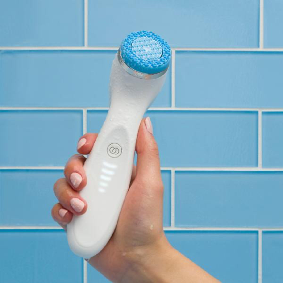 Hand holding a LumiSpa electronic device with a blue head against a blue tiled wall.