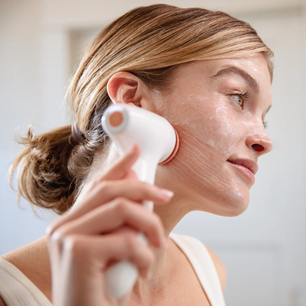 Woman using a white facial cleansing brush on her face.