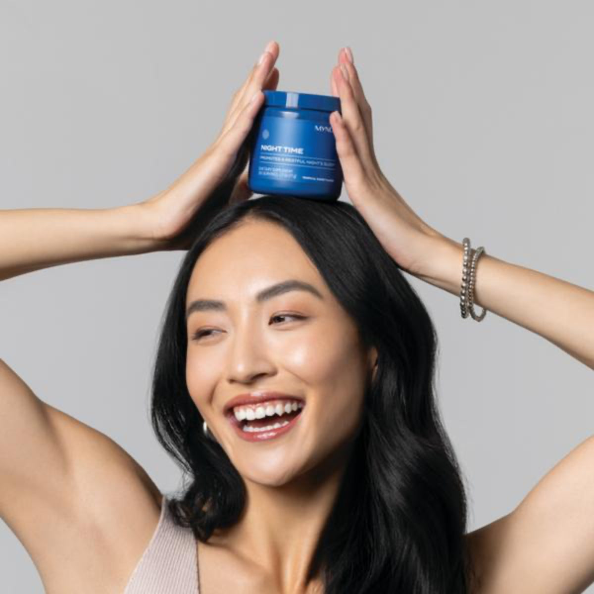 Woman holding a blue jar above her head against a gray background