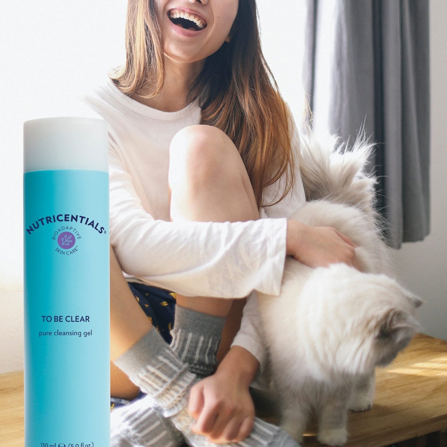 Woman sitting on a couch with a white dog, holding a bottle of 'Nutricentials' product.