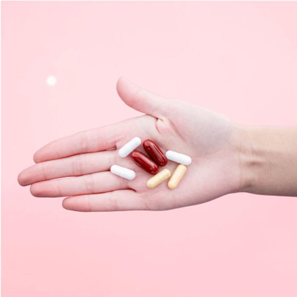 Hand holding various colored pills against a pink background