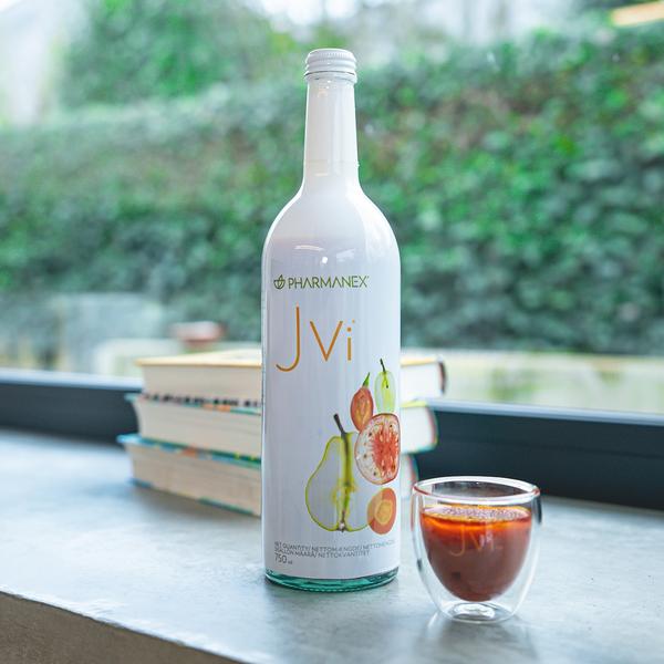 Bottle of JVi by Pharmanex on a table with a glass of red liquid in the foreground.