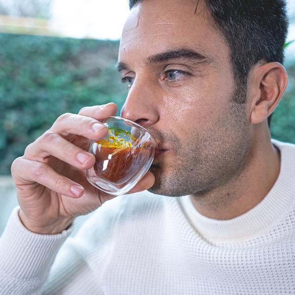 Man drinking from a small glass container outdoors